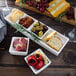 A table with a white rectangular tray filled with food, with a bowl of salsa and a white square bowl with olives and herbs.