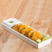 A white rectangular porcelain tray with fried plantains and sauce on a table.