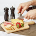 A person using a Franmara stainless steel knife to slice cheese on a cutting board.