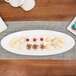 A white 10 Strawberry Street porcelain fish platter with cookies and cupcakes on a table.