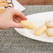 A hand holding a piece of food on a 10 Strawberry Street white porcelain fish platter.