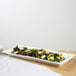 A 10 Strawberry Street white porcelain ridge platter with a plate of salad on a table.