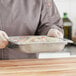 A person holding a Vollrath stainless steel steam table pan full of food.