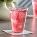 A clear plastic cup filled with a pink iced beverage, placed on a white coaster.