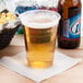 A Solo Ultra Clear PET plastic cup filled with beer on a table with a glass of beer and a bottle of beer.