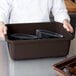 A chef holding a dark brown Cambro container full of plates.