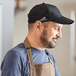 A man wearing a black Headsweats 5-panel cap and brown apron.