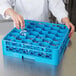 A hand placing a clear glass in a Carlisle blue glass rack with an extender.