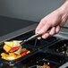 A hand holds a Sabert silver plastic serving fork filled with fruit over a container.