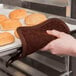 A hand using a San Jamar terry cloth pot holder to hold a tray of bread.