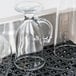 A clear glass jug sits on a black San Jamar Versa-Mat with a glass on it.