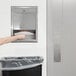 A person's arm reaching into a Bobrick paper towel dispenser.