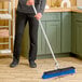 A man uses a Carlisle Sparta push broom with blue unflagged bristles to sweep the floor in a professional kitchen.