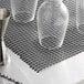 A group of glasses on a black San Jamar shelf liner.