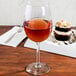 A Libbey wine glass filled with brown liquid on a table with a dessert.