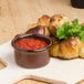 A Tuxton Artisan red ramekin filled with red sauce on a table with a plate of bread.