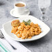 A Tuxton eggshell coupe square china pasta plate with a fork and a plate of pasta and a cup of coffee.