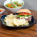 A Tuxton Artisan china pasta plate with a sandwich and chips on a table.