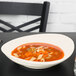 A Tuxton oval china bowl filled with soup with noodles and vegetables.