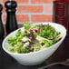 A Tuxton porcelain white slanted china bowl filled with salad on a table.