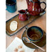 A table set with a tea set, including a Tuxton red pitcher and teacup, saucer, and spoon.