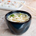 A bowl of soup with noodles and chopsticks in a Tuxton Artisan Night Sky china bouillon.