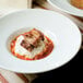 A Tuxton white porcelain china serving bowl with meat and mashed potatoes on a table.