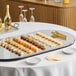 An oval rimless mirror food display tray measuring 24 by 48 inches, shown with assorted desserts arranged on top.