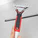 A hand holding a Unger ErgoTec window squeegee with a red and black handle.