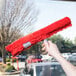 A hand using a Unger SmartColor red strip washer to clean a window.