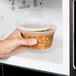 A hand holding a Pactiv translucent round deli container of beans in a microwave.
