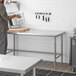 A man in a kitchen using a Regency stainless steel open base work table.