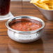 An American Metalcraft stainless steel Moroccan hammered bowl filled with salsa and chips on a table.