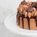 An American Metalcraft porcelain cake stand holding a chocolate cake with chocolate frosting and drizzle.