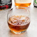 A glass of Arcoroc Salto Rocks with ice and brown liquid on a table in a cocktail bar.