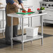 A man cutting green bell peppers on a Regency stainless steel work table with undershelf.