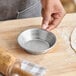A small round aluminum pie pan on a wooden surface next to a rolling pin and dough.
