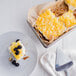 A plate of pineapple tidbits and blackberries next to a cake.