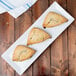 A rectangular white Thunder Group melamine plate with three scones on it.