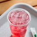A clear plastic lid with a straw slot on a cup filled with a red iced beverage.