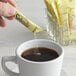 A hand pouring Splenda sugar substitute into a cup of coffee on a table in a café.