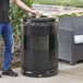 A man standing next to a black Rubbermaid Classics trash can with a drop top lid.