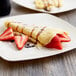 A Waring electric crepe maker plate with a crepe topped with strawberries and chocolate syrup.