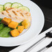 An Arcoroc Rondo salad plate with a plate of food and a fork and knife on a table.