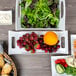 A white rectangular porcelain platter with handles holding a variety of food including fruit and vegetables.