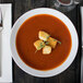 An Arcoroc Rondo coupe bowl filled with soup with croutons on top and silverware on a napkin.