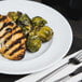 An Arcoroc Rondo dinner plate with chicken and brussels sprouts, a fork, and a knife.