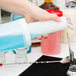 A hand pouring liquid from a white Carlisle Store 'N Pour container into a glass.