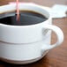 An Arcoroc stackable coffee cup filled with coffee and a straw on a counter.