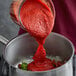 A person pouring Furmano's tomato puree into a pot.